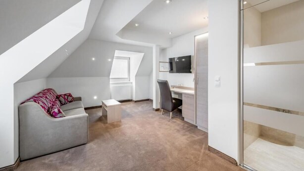 A modern loft bedroom with a sloped ceiling, a desk, a chair, and a sofa. - Hotel Garni Christine - Ischgl (Ischgl)