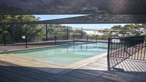 A swimming pool with a wooden deck and metal fencing, surrounded by trees. - TREE TOP BREEZE - SUNRISE AT 1770 (AGNES WATER)