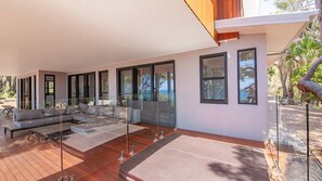 A modern outdoor living space with a built-in sofa and dining area, large windows, and a wooden deck. - TREE TOP BREEZE - SUNRISE AT 1770 (AGNES WATER)