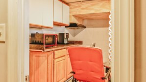 A compact kitchen with wooden cabinets, a microwave, a coffee maker, and a red chair. - Essex Smart Stay (Essex)