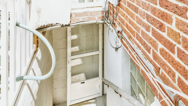 A narrow stairwell with a metal handrail, a door with a metal handle, and a brick wall. - Essex Smart Stay (Essex)
