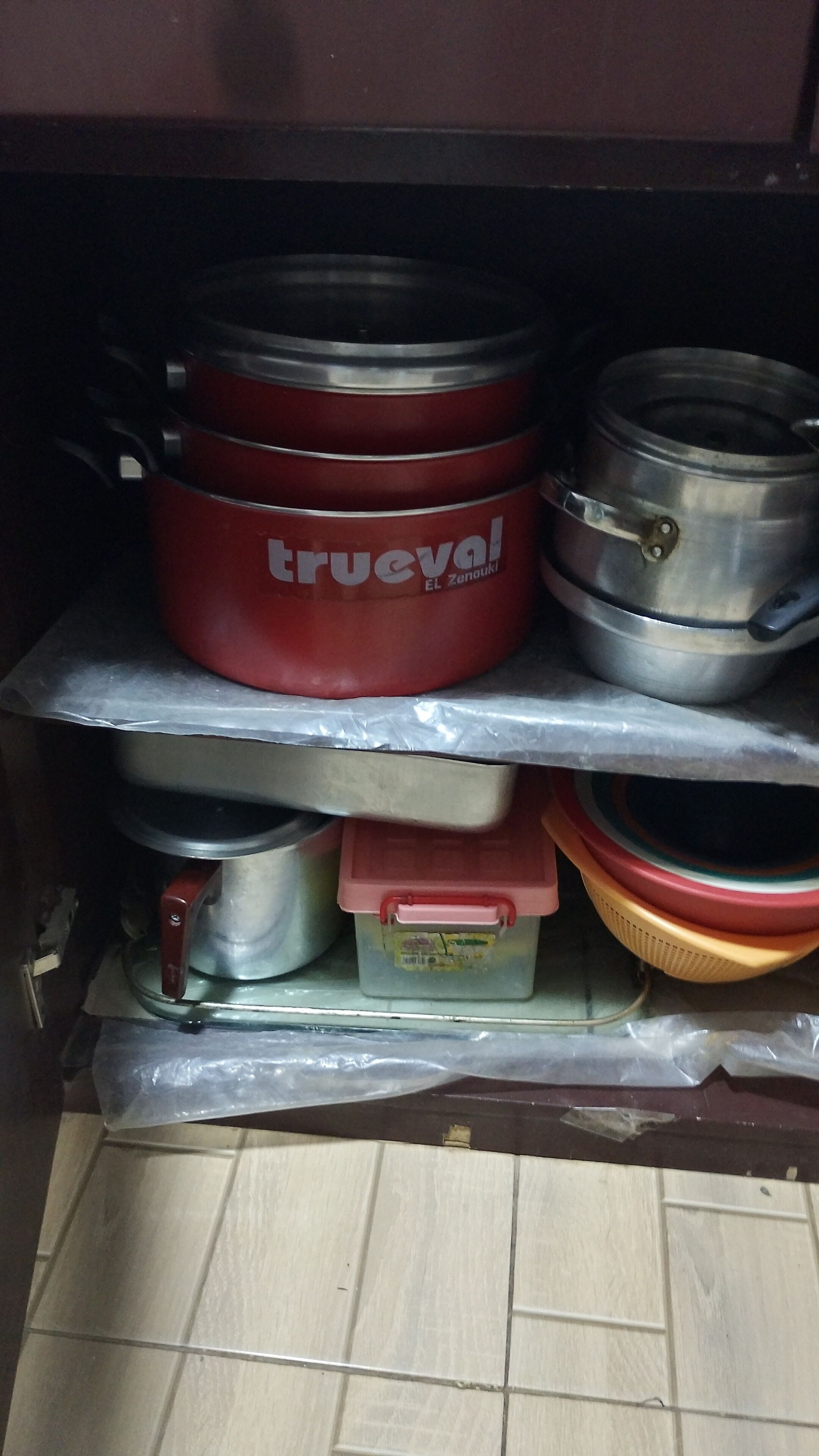 Een keukenkastje met diverse kookpannen, waaronder een rode pan met de aanduiding 'trueval' en een roestvrijstalen pan.