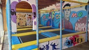 An indoor play area with a climbing wall, a trampoline, and a basketball hoop.