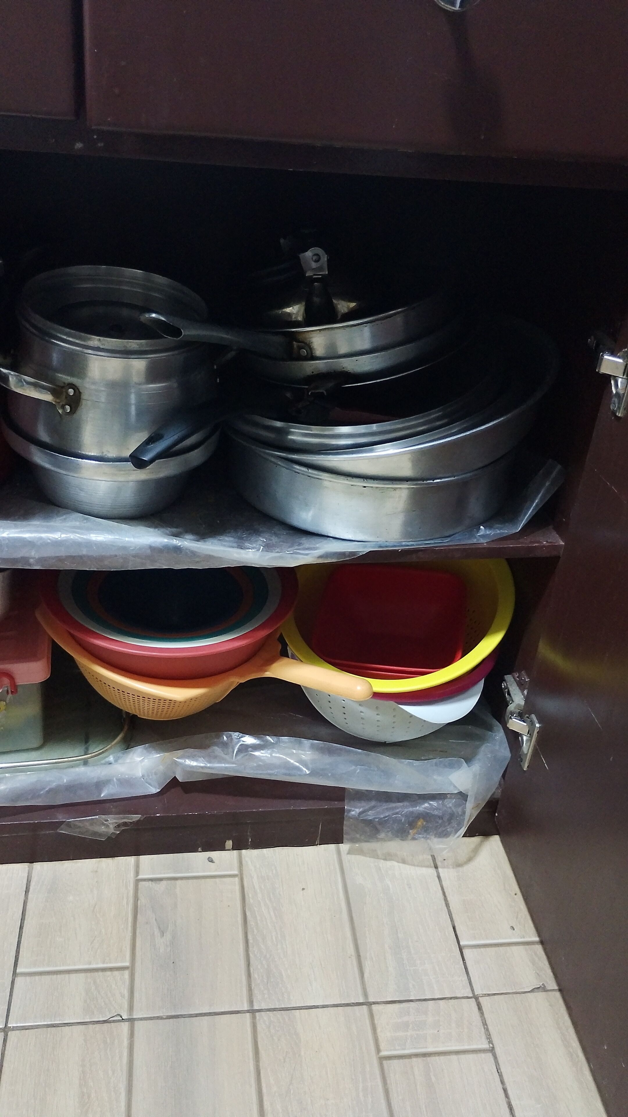 Ein Küchenschrank mit Edelstahlkochgeschirr, Plastikbehältern und einer Plastiktüte.