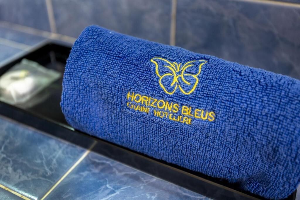 Toalha azul com bordado e um logotipo de borboleta, sobre um chão de azulejos.