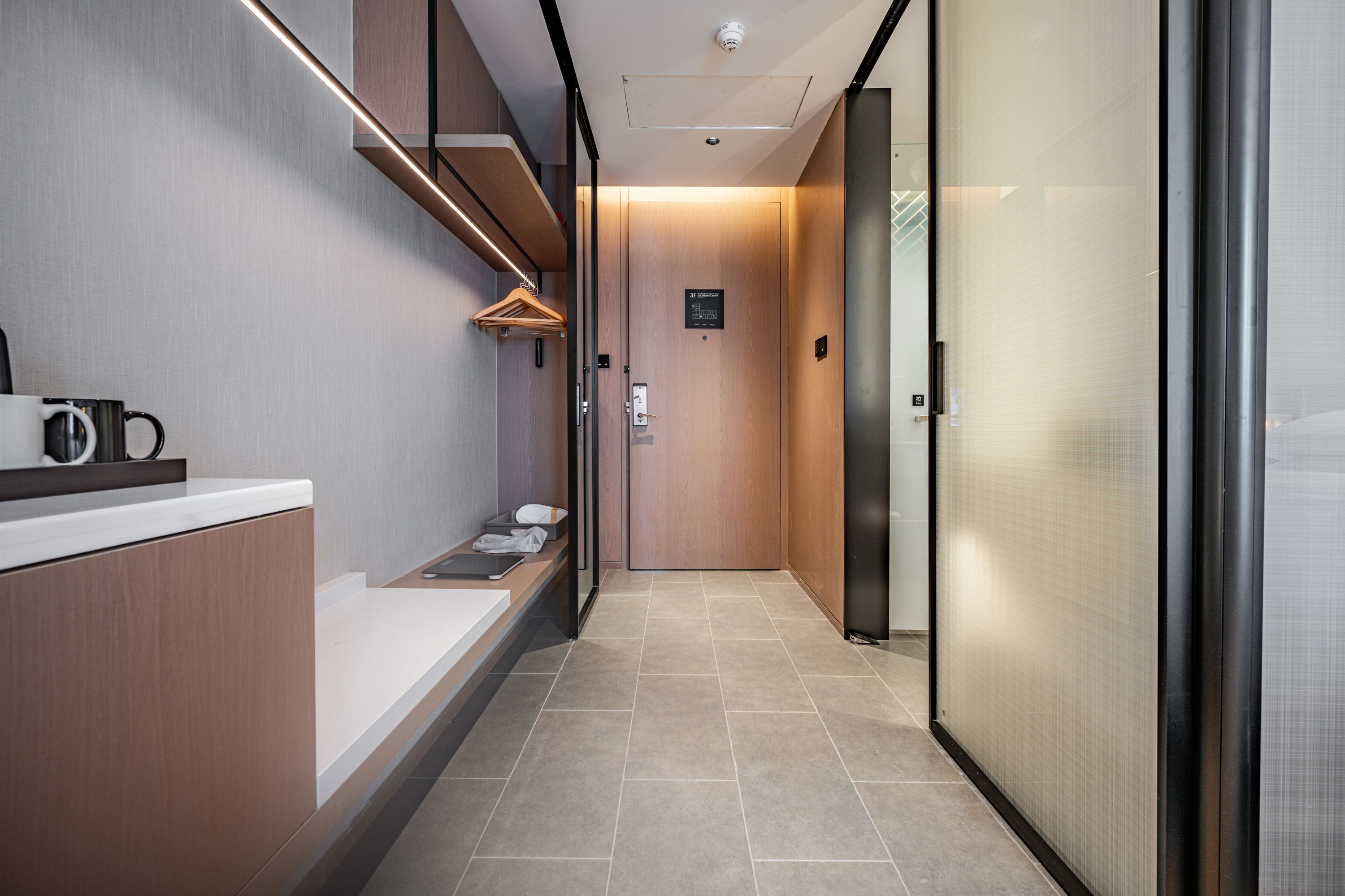 Un corredor moderno de hotel con una recepción, un perchero y una puerta de ascensor de vidrio.