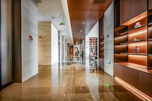 Un pasillo de hotel con piso de mármol pulido, paneles de madera en el techo y una exhibición de objetos decorativos en estanterías.