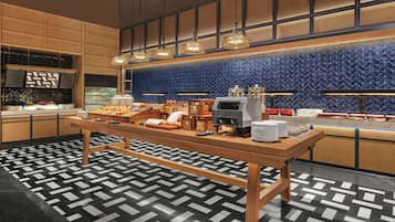 Una mesa de buffet con diversos alimentos, una máquina de café y un suelo estampado.