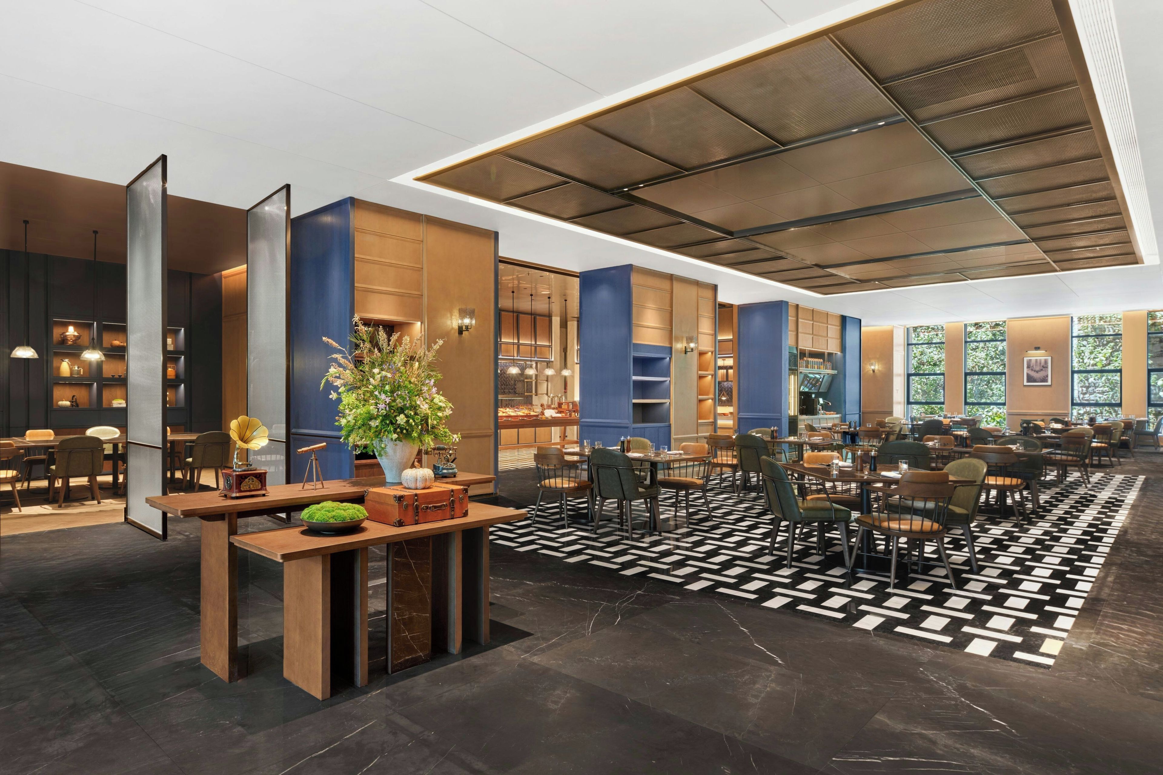 A modern hotel lobby with a central reception desk, seating area, and a large window providing a view of the outdoors.