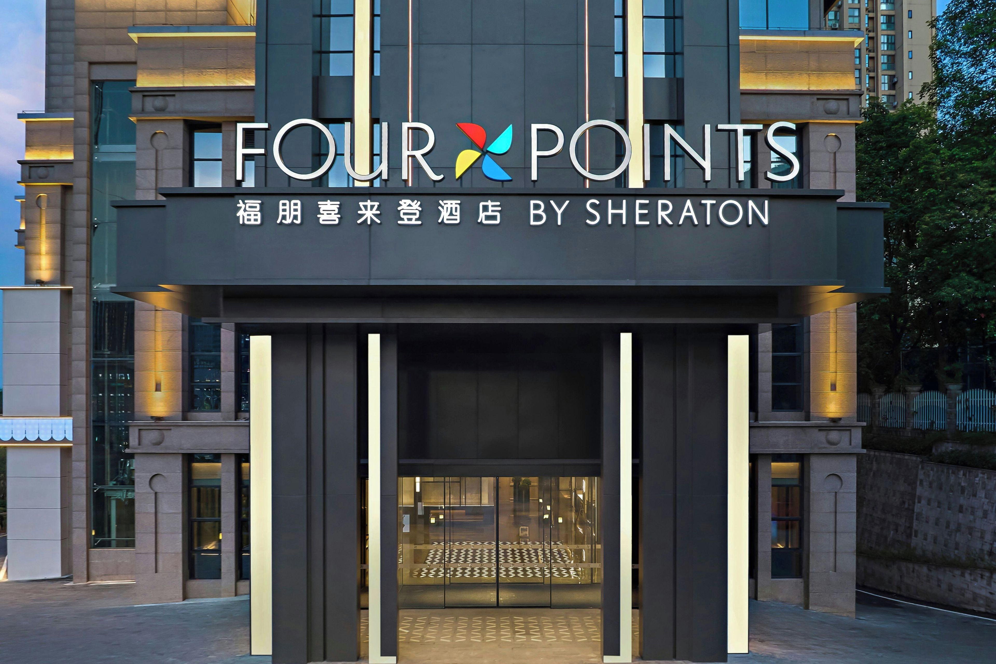 Entrada de hotel con diseño moderno, destacando un letrero grande 'FOUR POINTS' y un logotipo con diseño de molinete.
