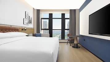 Habitación de hotel con una cama grande, un escritorio, una silla, un televisor y ventana con vista a la ciudad.
