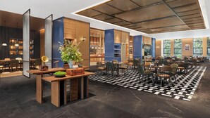 En moderne hotellobby med et centralt siddeområde, en stor plante og et mønstret gulv.