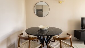 A round dining table with a central decorative object, surrounded by woven chairs, against a plain wall with a mirror and wall-mounted lights. - Take Five on the Green (London)