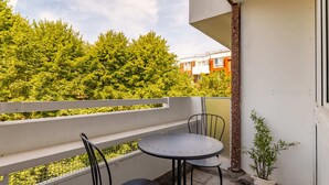 A balcony with a table and chairs, a potted plant, and a view of a tree-lined street. - Take Five on the Green (London)