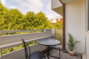 A balcony with a table and chairs, a potted plant, and a view of a tree-lined street. - Take Five on the Green (London)