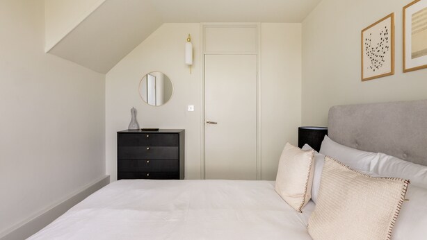 A bedroom with a bed, a dresser, a door, and a wall-mounted lamp. - Take Five on the Green (London)