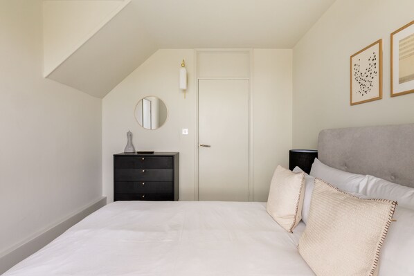 A bedroom with a bed, a dresser, a door, and a wall-mounted lamp. - Take Five on the Green (London)
