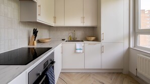 A modern kitchen with white cabinets, a black induction cooktop, a stainless steel sink, and a herringbone-patterned floor. - Take Five on the Green (London)