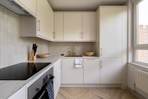 A modern kitchen with white cabinets, a black induction cooktop, a stainless steel sink, and a herringbone-patterned floor. - Take Five on the Green (London)