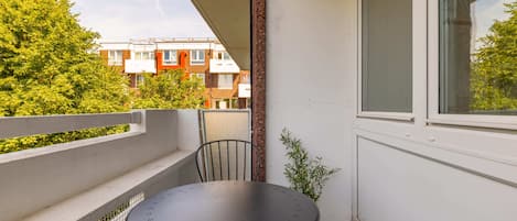 A balcony with a table and chairs, a potted plant, and a view of a residential building.