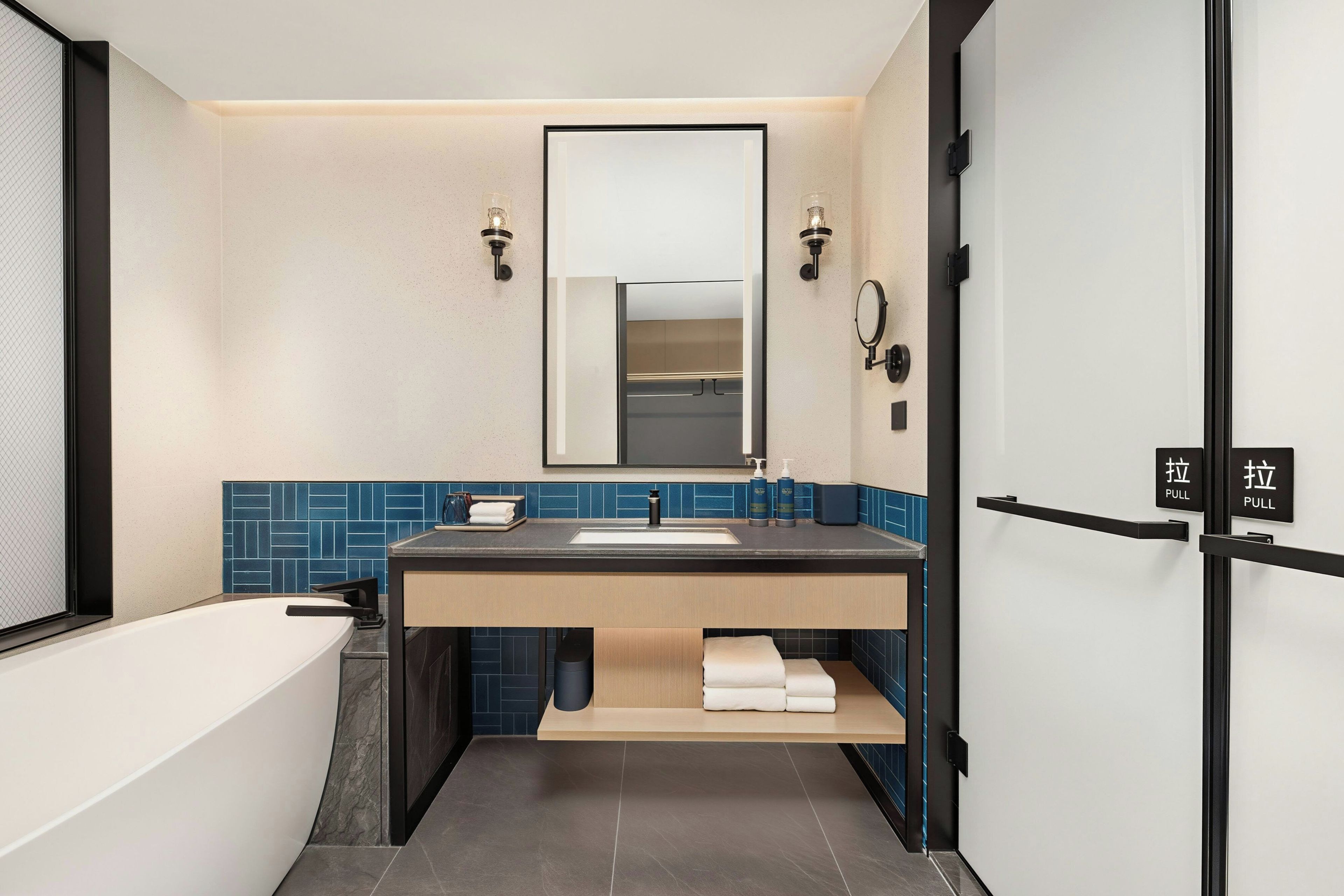 Un baño moderno con bañera, lavamanos y espejo. Hay dos dispensadores de toallas y una repisa con toallas.