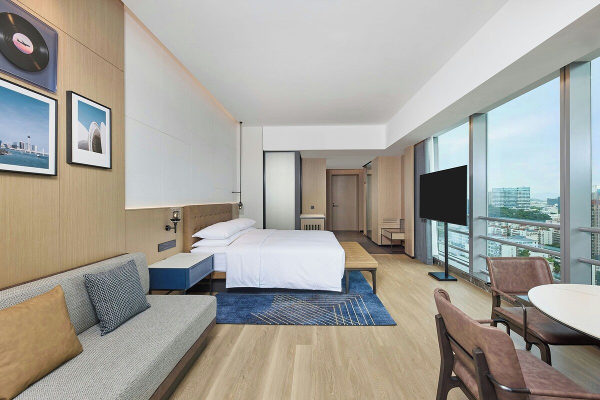 Una habitación de hotel moderna con una cama grande, un sofá, un escritorio y un televisor.