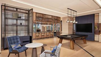 A modern lounge area with a pool table, seating, and a bar area with bottles.