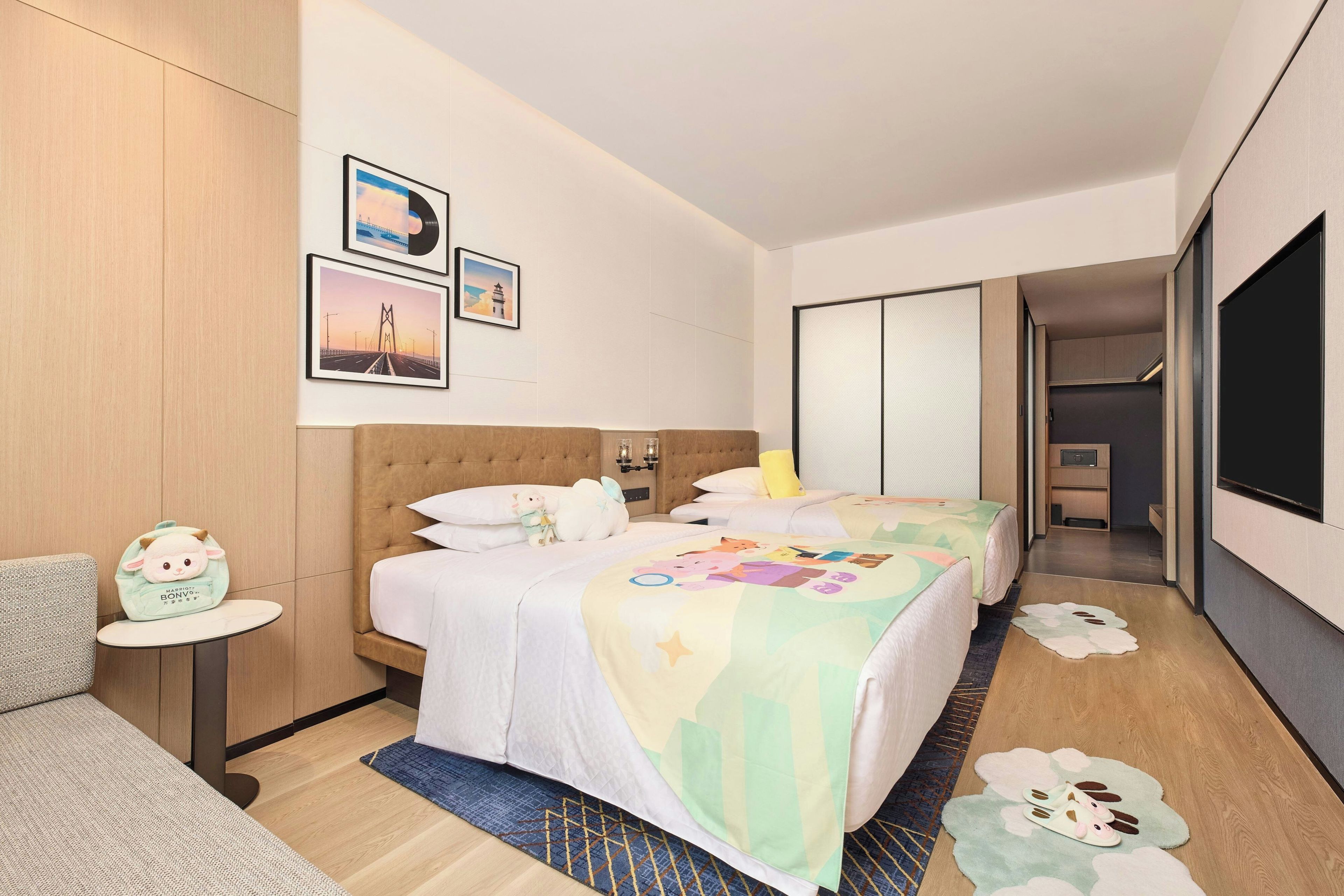 A hotel room with two beds, a sofa, a small table, and a wall with framed pictures.