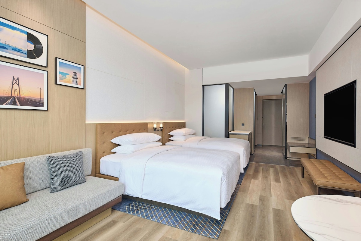Habitación de hotel con dos camas, un sofá, un televisor y obras de arte en la pared.