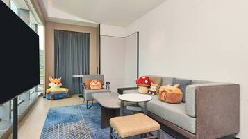 A modern hotel room with a sofa, a small table, a flat-screen TV, and a window with curtains.
