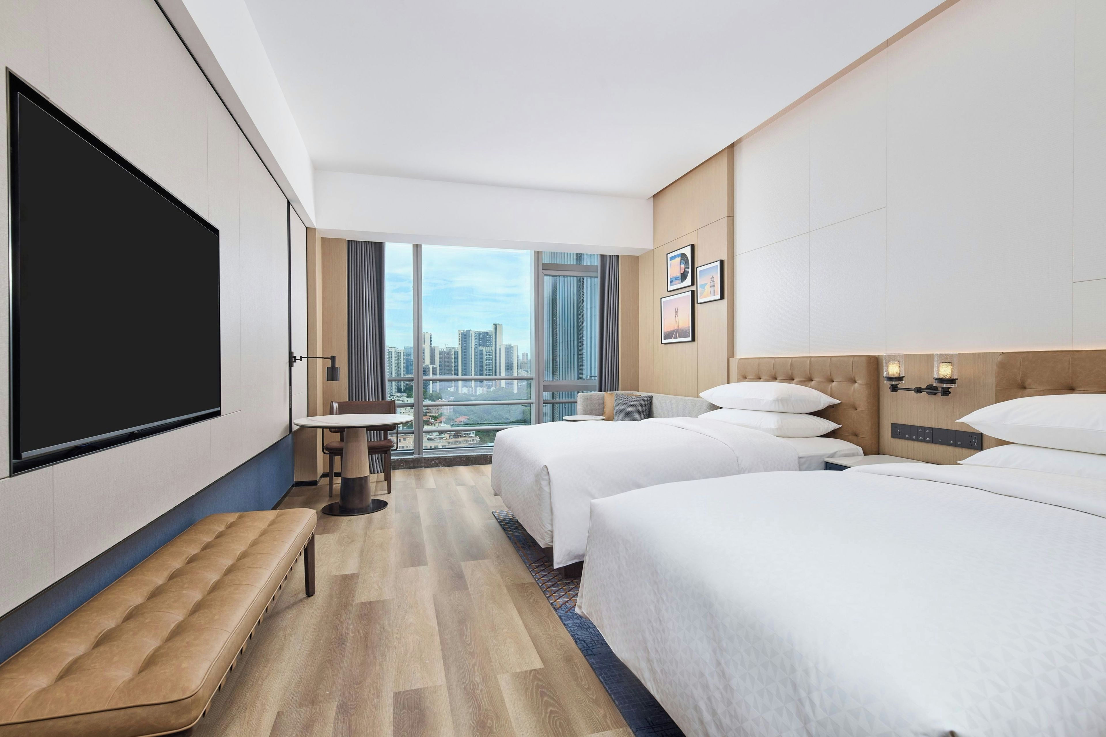 A hotel room with a city view, two beds, a seating area, and a flat-screen TV.