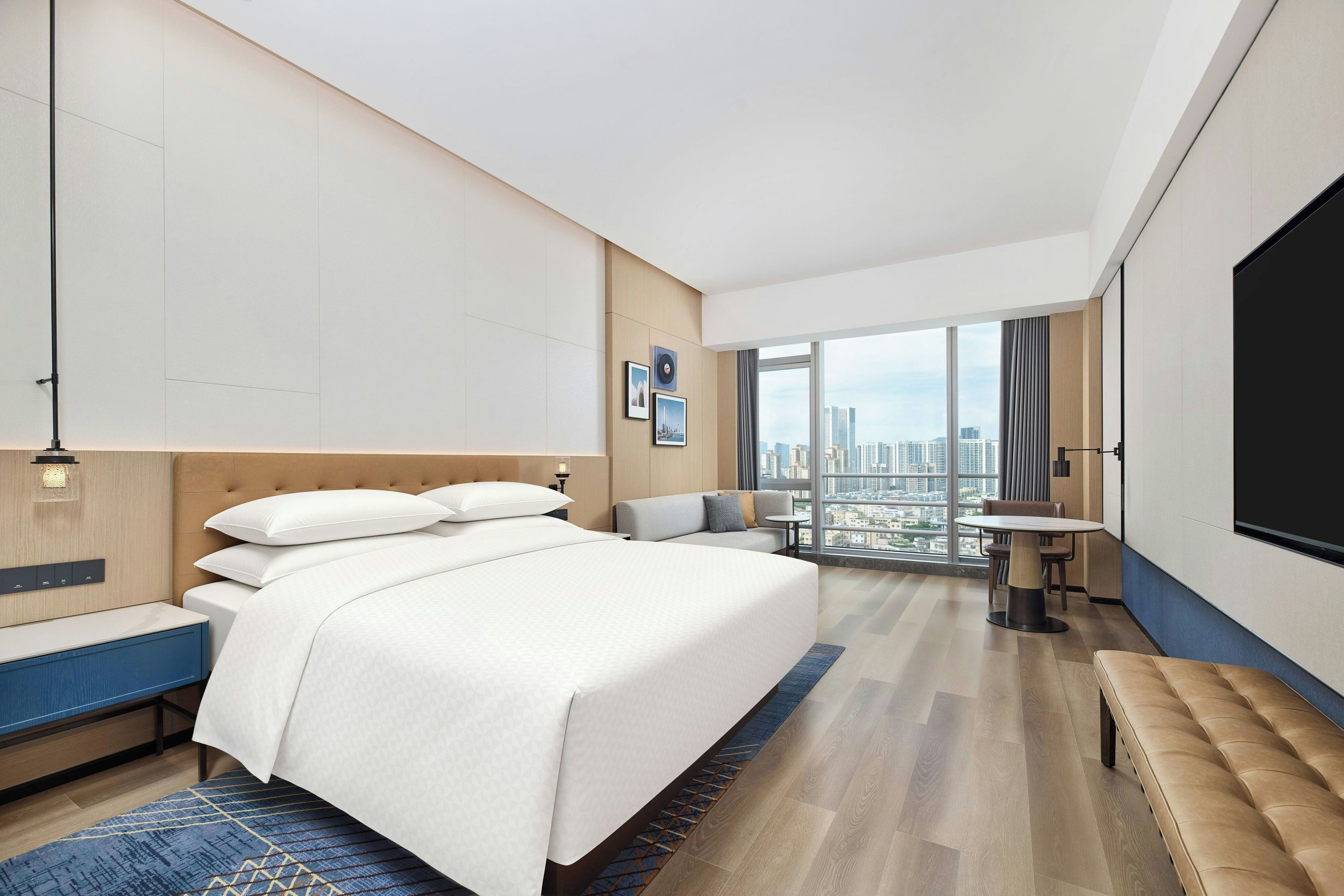 A modern hotel room with a large bed, a seating area, and a city view.