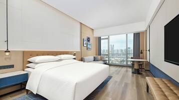 A modern hotel room with a large bed, a seating area, and a city view.