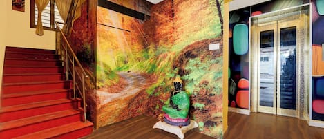 A staircase with red steps leading to a landing, a wall with a mural, and a statue of a seated figure.
