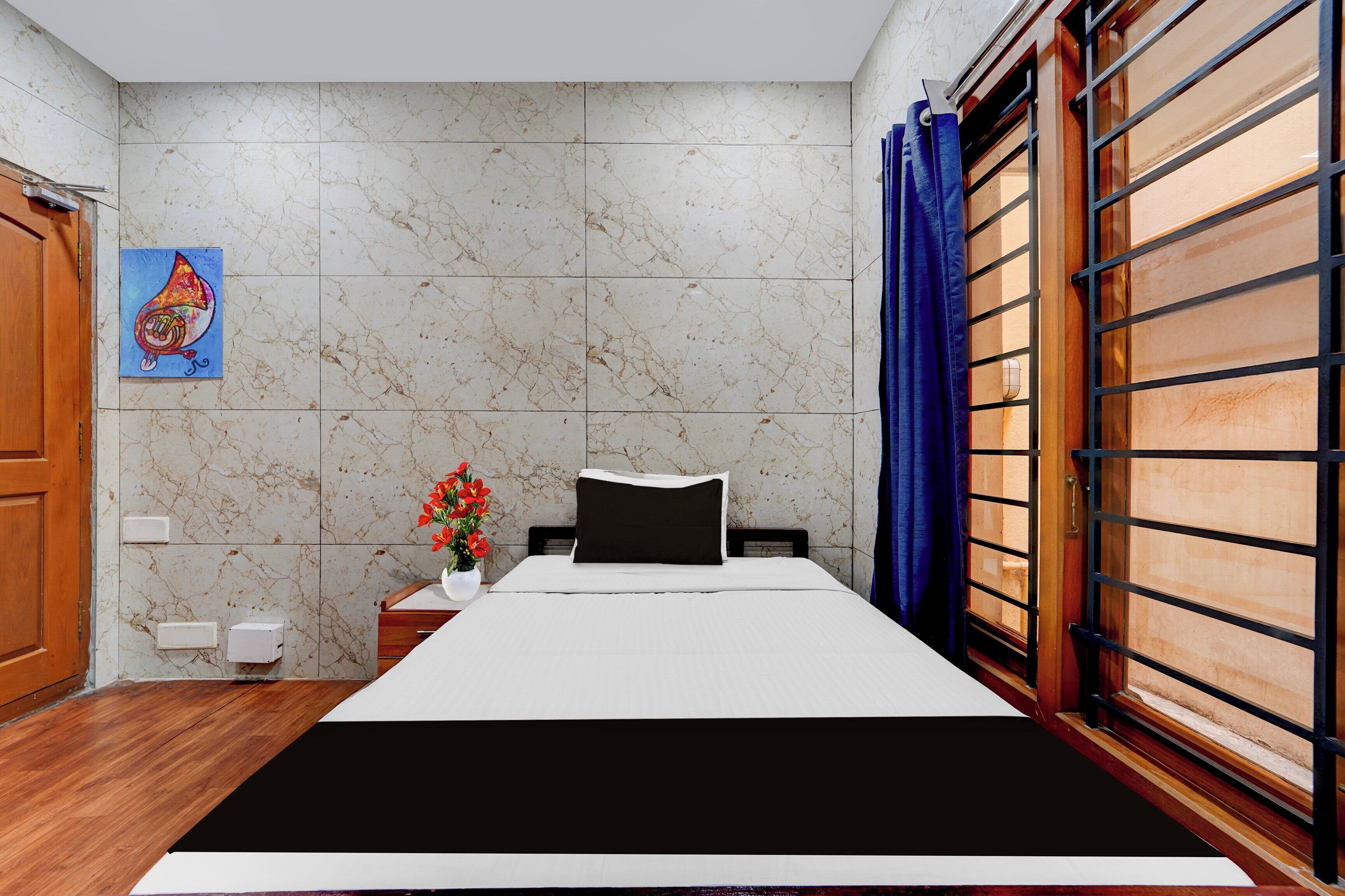 A hotel room with a bed, a nightstand, a wall-mounted light switch, and a window with a curtain.