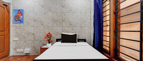 A hotel room with a bed, a nightstand, a wall-mounted light switch, and a window with a curtain.