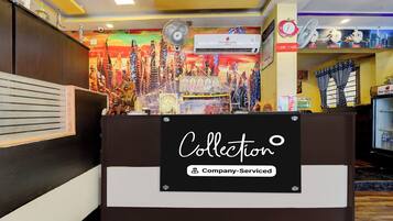 A hotel reception desk with a 'Collection' sign, a clock, and a cityscape mural in the background.