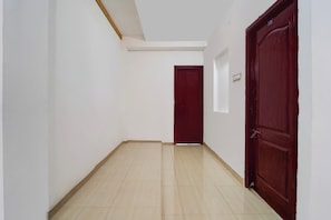 A narrow hallway with a wooden floor, white walls, and a red door at the end. - Super Collection O Race Course Road (Coimbatore)