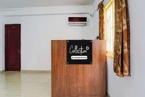 A room with a wooden podium, a red door, a window with patterned curtains, and an air conditioning unit on the wall. - Super Collection O Race Course Road (Coimbatore)