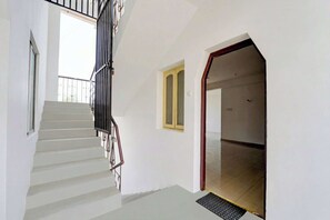 Una escalera con barandilla metálica que lleva a una plataforma, una puerta con marco amarillo y una ventana con barandilla.