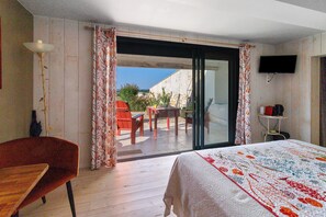 Una camera d'albergo con un letto, una sedia, un tavolo e una porta finestra scorrevole che dà su uno spazio all'aperto.