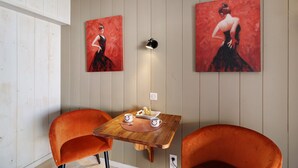 Une pièce avec deux fauteuils orange, une table en bois sur laquelle se trouve un plateau avec de la nourriture et des boissons, et deux tableaux accrochés au mur.