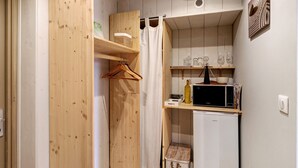 Une cuisine compacte équipée d’un four à micro-ondes, d’un petit réfrigérateur et d’une étagère en bois où sont rangés des verres.