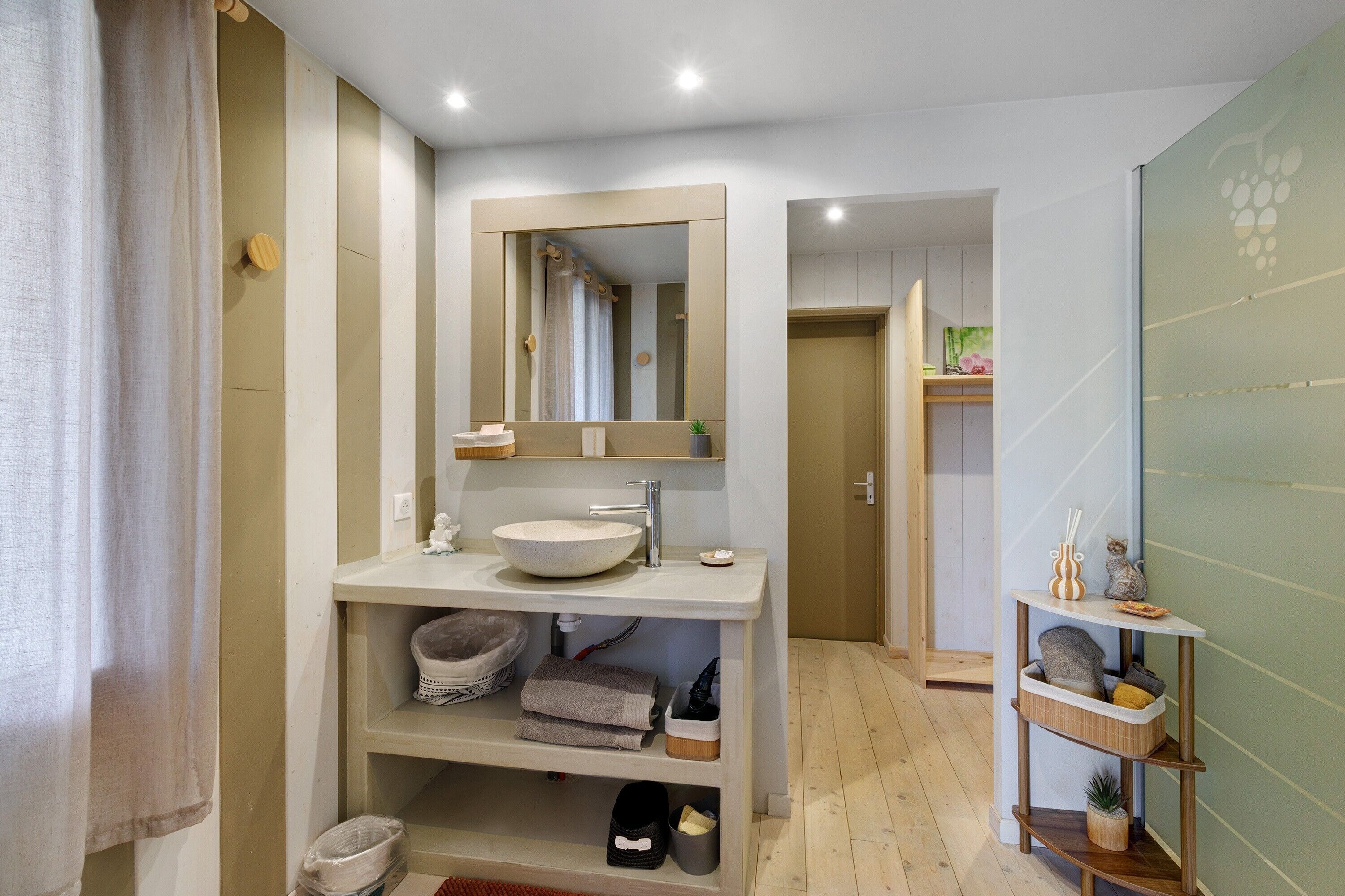 A modern bathroom with a large mirror, a sink, and a shelf with towels and toiletries.