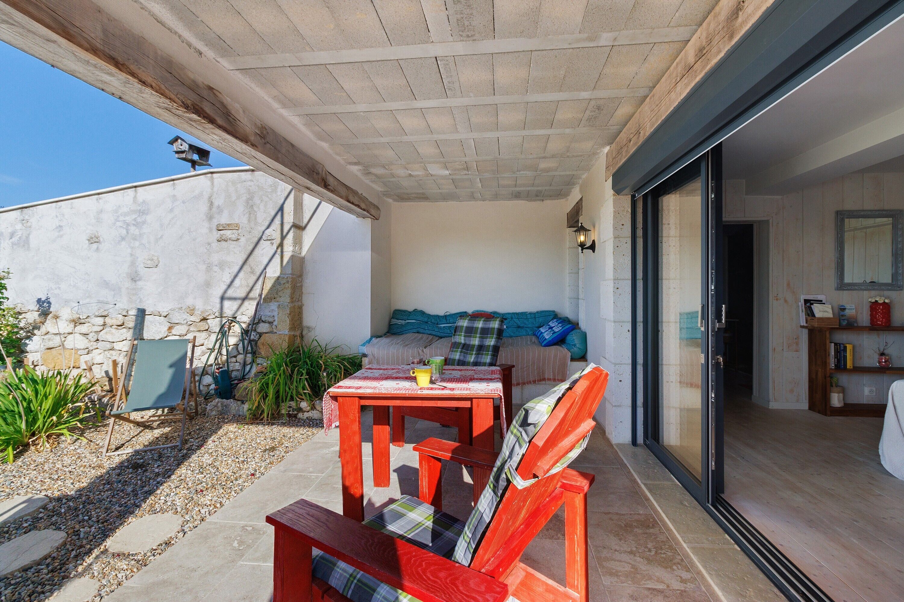 An outdoor patio with a table and chairs, a stone wall, and a covered area with a sofa.