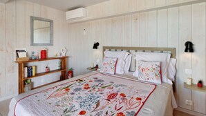 Une chambre à coucher avec une tête de lit en bois, une courtepointe à motifs floraux, une table de chevet avec une lampe et une étagère avec des livres et des objets décoratifs.