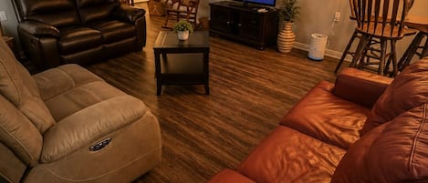 A living room with a leather sofa, a recliner, a television, and a lamp.