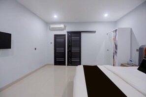 A hotel room with a bed, a flat-screen TV, a wardrobe, and a door with a handle.