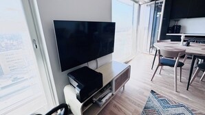 Uma sala de estar moderna com televisão de tela plana, piso de madeira e uma grande janela com vista para a cidade.