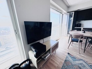 Ein modernes Wohnzimmer mit Flachbildfernseher, Holzboden und einem großen Fenster mit Blick auf die Stadt.
